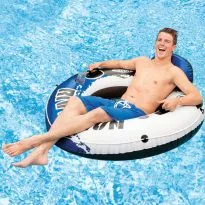 
A young man is happily reclining in a blue and white inflatable Intex River Run tube in a swimming pool, with a drink in a cup holder and his arm resting on the side.