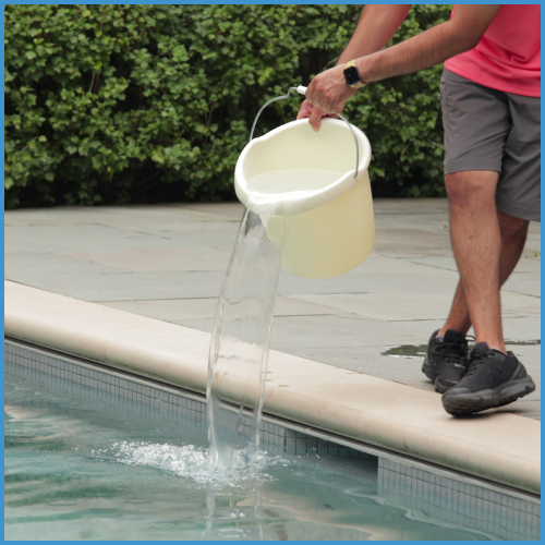 Pouring a bucket of pool shock into the water during pool opening.